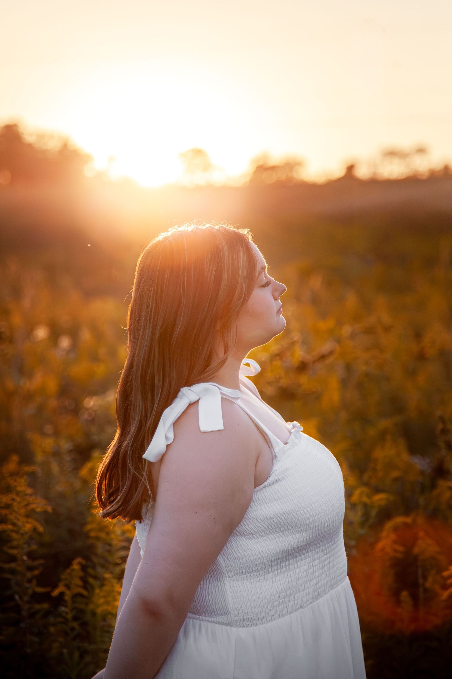 Side profile in a white dress, backlit by the setting sun.