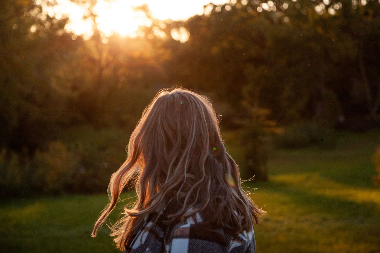Sunlight catches a person's hair as they turn away in a field.