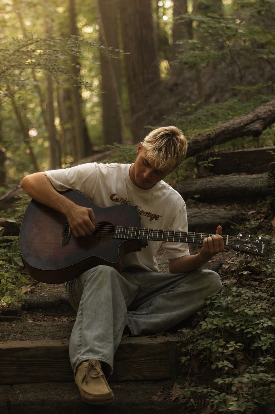 A guitarist sitting on woodland steps, focused on playing.